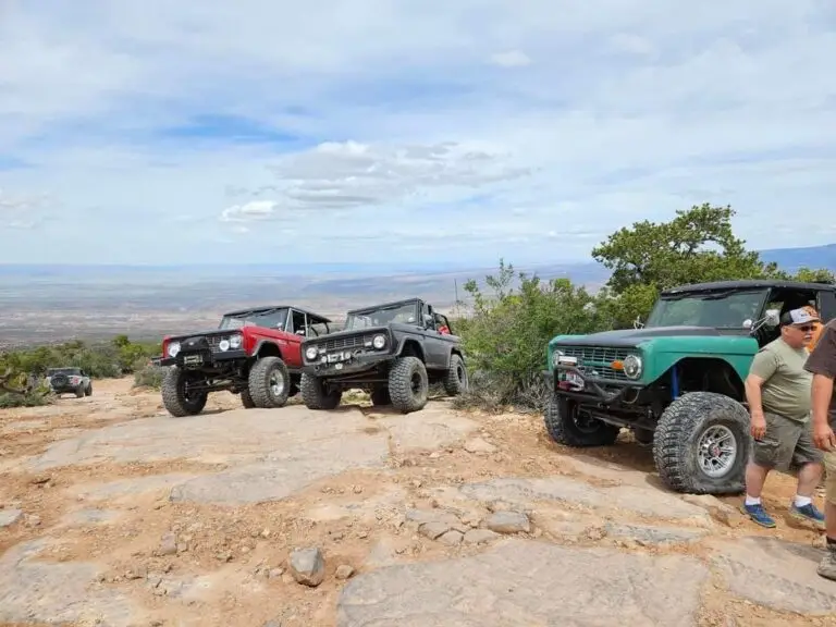 Red, black and green early Broncos parked at a high desert overlook with people nearby