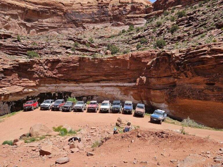Line of vehicles parked beneath a large red rock alcove