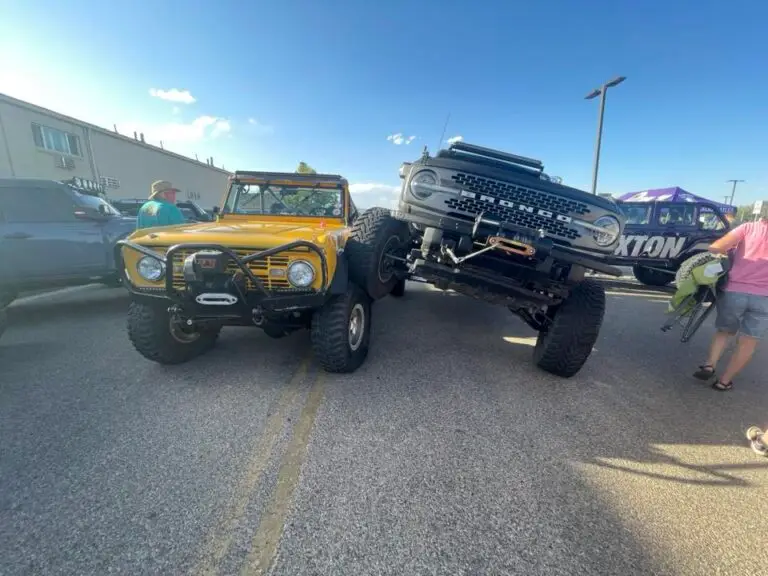 Two Broncos, one yellow and one black, at a meetup on a paved road