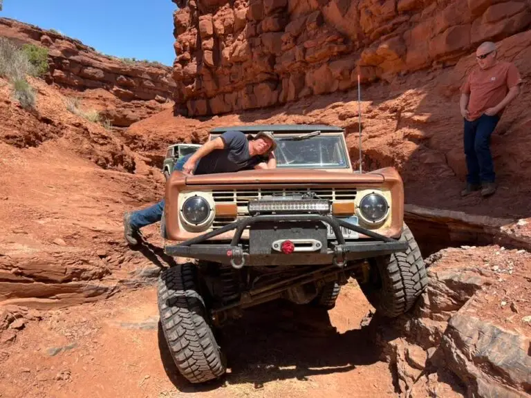 Early Bronco crawling over a red rock ledge with people nearby