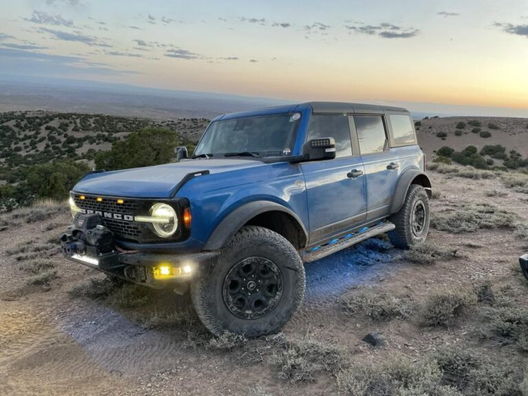 Blue Bronco with glowing fog lights on a desert overlook at sunset
