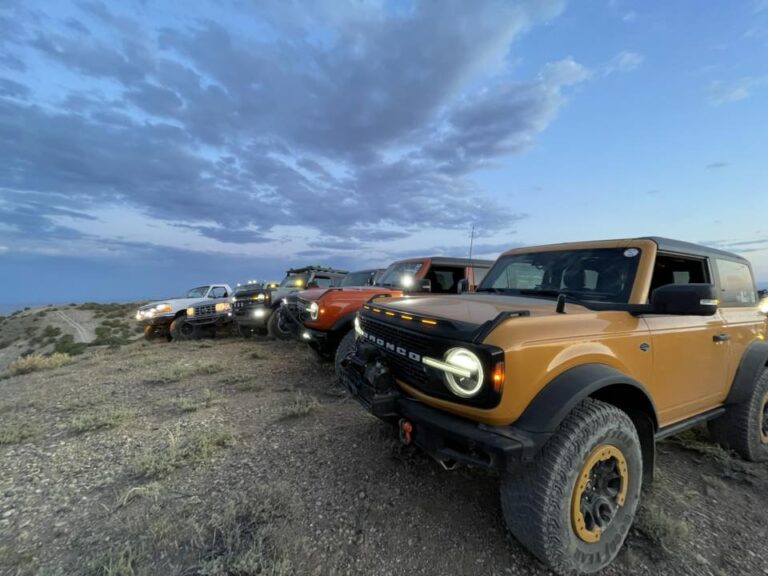 Yellow Bronco and other vehicles lined up on a rocky overlook at dusk