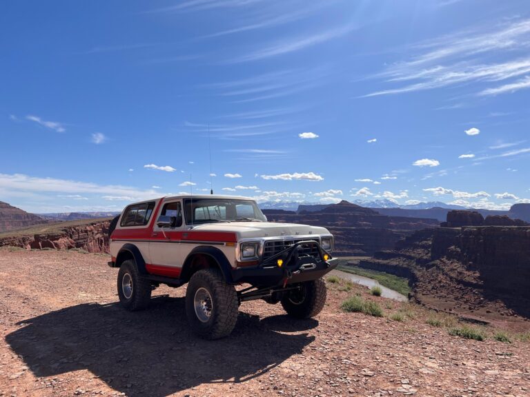 White and red early Bronco on slickrock with a canyon behind it