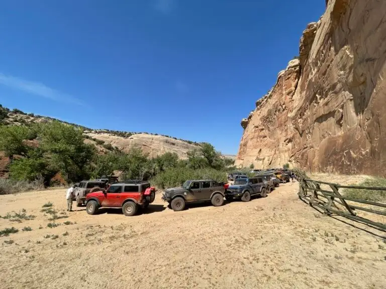 Vehicles parked along a dirt road beside a sandstone cliff