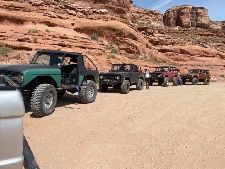 Green early Bronco leading a line of vehicles on a dirt road through red rock country