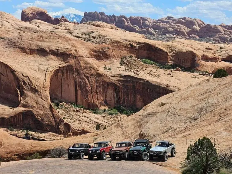 Row of Broncos parked at the base of a red rock canyon